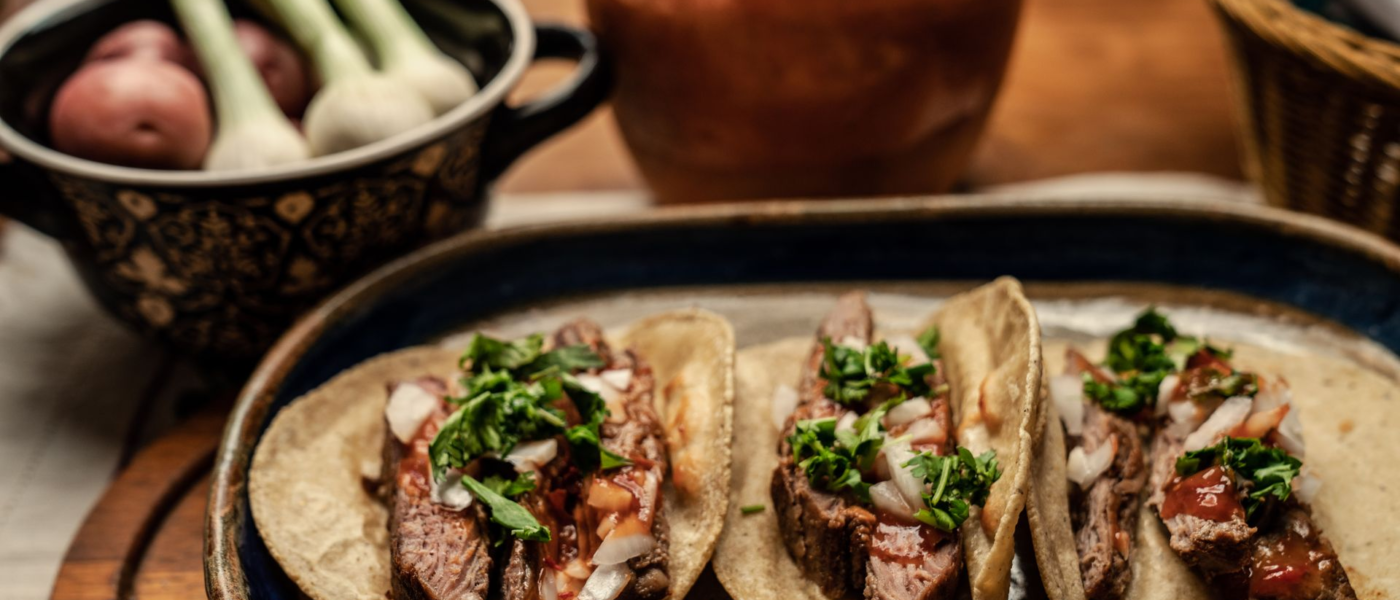 Sliced grilled carne asada steak on corn tortillas topped with onion, cilantro, and salsa
