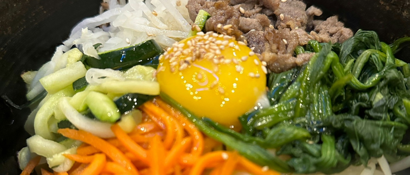 Dolsot bibimbap in a hot stone bowl with julienned vegetables, marinated beef, and a raw egg yolk on top