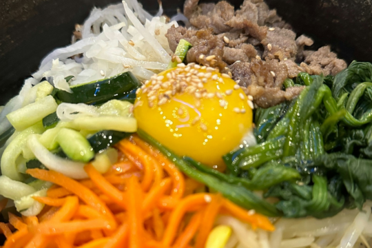 Dolsot bibimbap in a hot stone bowl with julienned vegetables, marinated beef, and a raw egg yolk on top