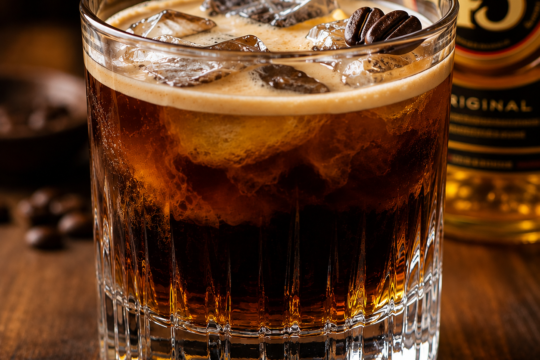 Iced Carajillo in a rocks glass with a thick foamy top over dark espresso and Licor 43, ice cubes and a coffee bean garnish