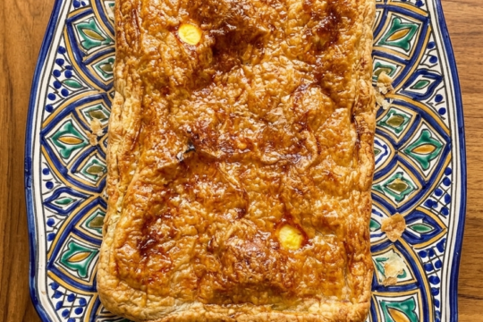 Golden baked empanada gallega de atún on a decorative plate, sliced into squares