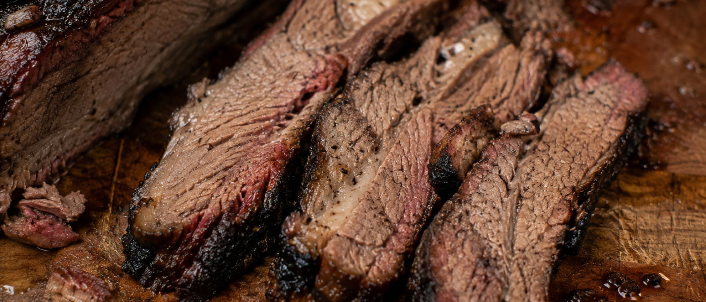Slices of smoked beef brisket showing a deep pink smoke ring and dark peppery bark, fanned out on a wooden cutting board
