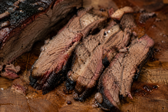 Slices of smoked beef brisket showing a deep pink smoke ring and dark peppery bark, fanned out on a wooden cutting board