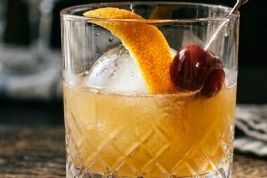 Whiskey Sour in a rocks glass over ice, garnished with an orange peel twist