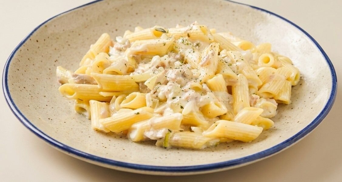 Penne pasta coated in a creamy tuna and Parmesan sauce, served on a blue-rimmed plate