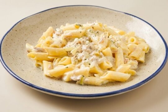 Penne pasta coated in a creamy tuna and Parmesan sauce, served on a blue-rimmed plate