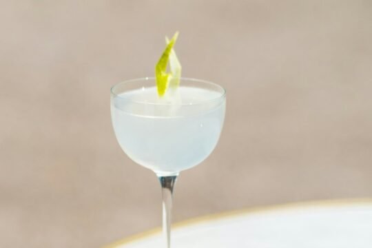 A pale, chilled Daiquiri in a coupe glass garnished with a lime twist on a marble table