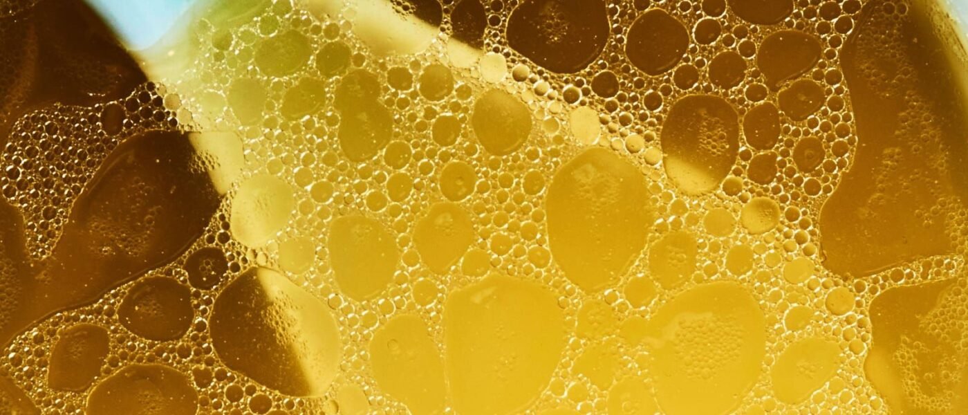 Overhead close-up of clear, golden homemade chicken stock in a white bowl, small beads of chicken fat floating on the surface and the handle of a blue-and-white ceramic spoon resting in the broth